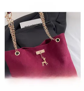 Detail view of burgundy faux suede tote bag featuring gold chain handle and deer charm