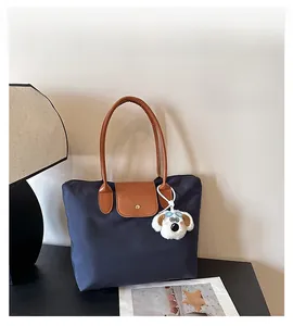Detail of navy nylon tote bag showing leather handles and white plush dog charm