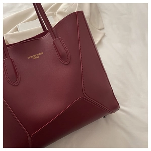 Détail du sac cabas bordeaux avec texture cuir et logo en lettres dorées embossées