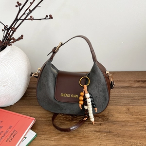 Minimalist half-moon crossbody bag in grey suede and brown leather on wooden desk