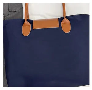 Detail of navy nylon tote bag showing brown leather handle and flap stitching