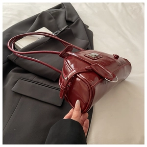 Detail of burgundy patent leather baguette bag with silver hardware on a black blazer