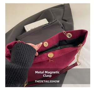 Detail of burgundy suede tote with magnetic buckle and golden deer emblem