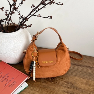 Vintage brown suede crescent crossbody bag with wooden bead charm on a wooden table