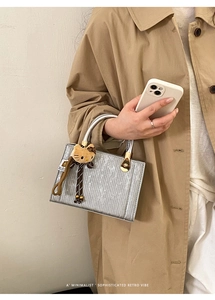 Detail of silver textured rectangular handbag with metallic handle and plush charm