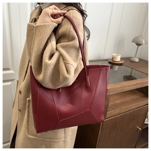 Grand sac cabas en cuir bordeaux porté avec un manteau kaki dans un décor minimaliste