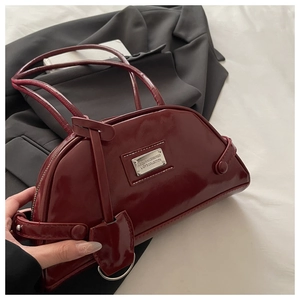 Detail of dark red patent leather dumpling bag with silver metal plaque on black blazer