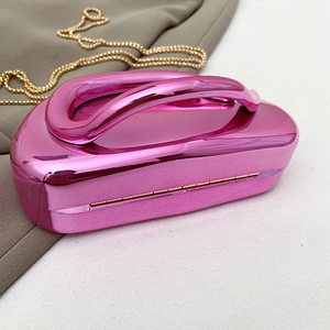 Detail of metallic rose red hard shell clutch bag with gold chain strap and integrated handle