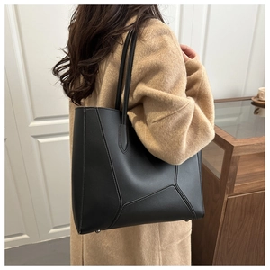 Detail of minimalist black tote bag with geometric stitching paired with a tan wool coat