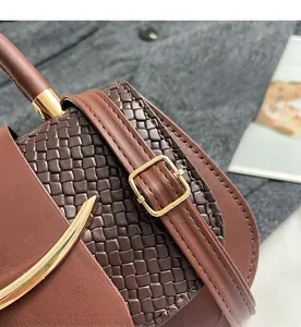 Detail of brown leather handbag featuring woven texture and gold metal buckle strap