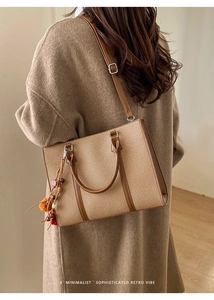 Retro khaki tote bag with brown leather trim and tassel charm shown on a shoulder