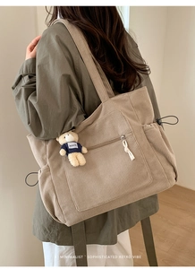 Detailed back view of a beige corduroy tote bag with side drawstring and bear charm