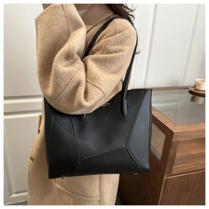 Détail d'un sac cabas noir en cuir avec surpiqûres géométriques et lettrage doré