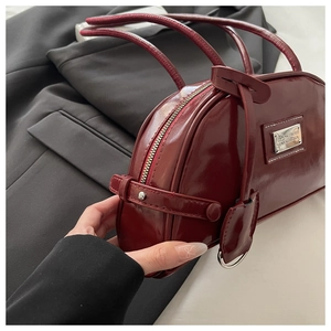Close-up of a burgundy patent leather hobo bag featuring metal logo and zipper details