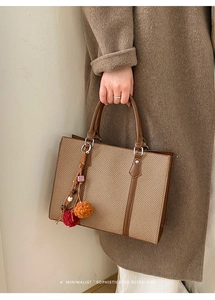 Nahaufnahme der gewebten Retro-Tasche mit Ledergriffen und farbigen Plüsch-Anhängern