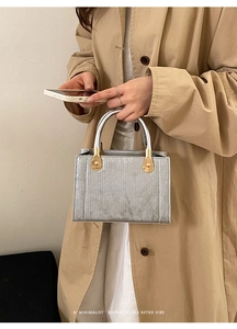 Détail d'un sac à main argenté avec texture rayée verticale et poignée métallique