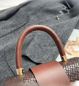 Detail of woven brown leather handbag handle with sleek gold metallic hardware accents