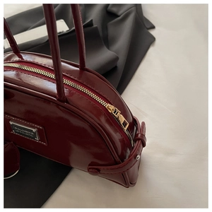 Detail of dark burgundy glossy leather bag featuring golden metal zipper and buckle