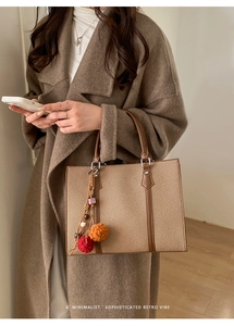 Detail of woven tote bag with leather handles and colorful pompom charm decoration
