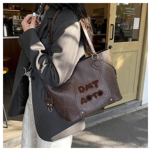 Close-up of a coffee brown tote bag with fuzzy DMT AOTO lettering and gold hardware