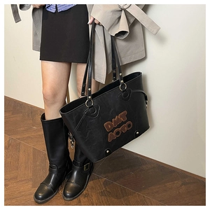 Close-up of black leather tote bag with brown velvet lettering and golden metal hardware