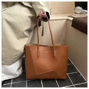 Détail d'un cabas en cuir marron avec coutures géométriques et lettrage du logo doré