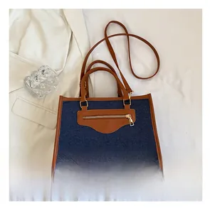 Detalle de bolso tote denim con ribete de cuero marrón y cremallera metálica dorada