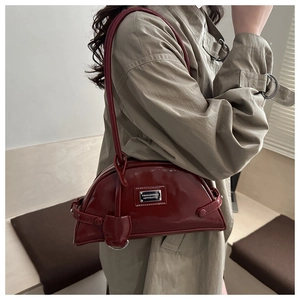 Detail of burgundy patent leather shoulder bag showing glossy texture and metal plaque