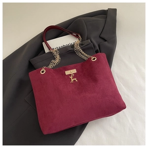 Detail of burgundy corduroy tote with gold chain strap and deer charm on a grey suit