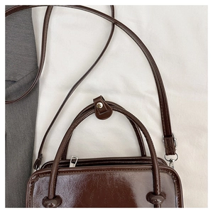 Detail view of smooth dark brown patent leather shoulder bag with silver buckle strap