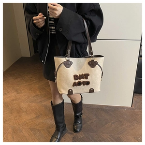 Detail of beige tote bag showing brown leather handles and DMT AOTO textured letter patch