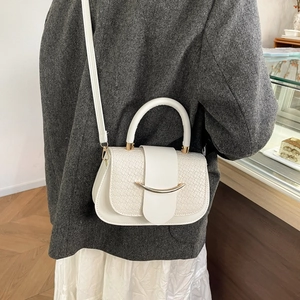 Detailed shot of white textured weave handbag with gold buckle on a grey coat
