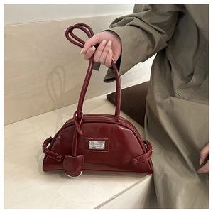 Detail of burgundy patent leather Boston bag with metal logo and sleek top handles