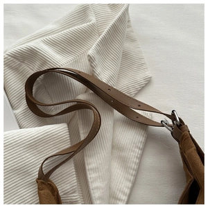 Detail of adjustable leather strap and metal buckle on a brown suede shoulder bag