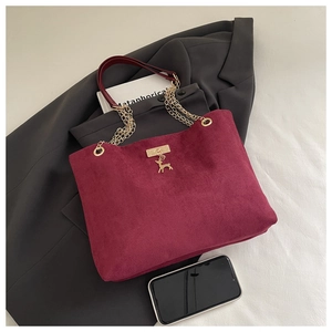 Detail of burgundy suede tote bag featuring golden chain strap and deer pendant