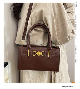 Dettaglio borsa tote marrone vintage con fibbia a cuore dorata su trench coat beige
