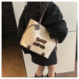 Detail of a beige tote bag with brown plush letter patches and leather shoulder straps
