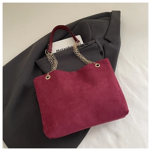 Detail of burgundy matte suede tote bag featuring elegant golden chain straps on a grey blazer