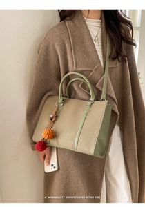Detail of green leather trim and beige woven texture tote with a plush ball charm
