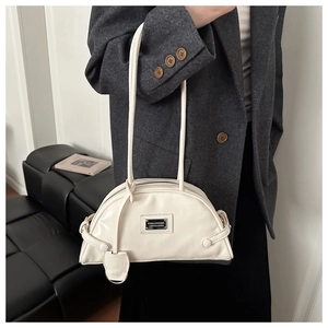 Close-up of beige crescent moon shoulder bag with metallic logo and leather tassel