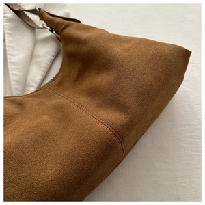 Detailed macro view of the caramel brown suede texture and fine stitching on the handbag