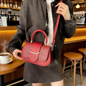 Detail of red crossbody handbag with woven texture and gold metal accent in a cafe