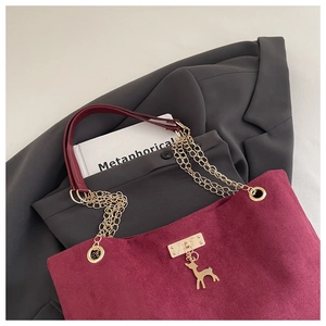 Detail of burgundy corduroy tote bag featuring gold hardware and a deer charm pendant