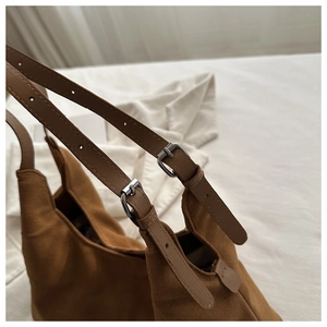 Detail of brown suede shoulder bag showing silver metal adjustment buckle and leather strap