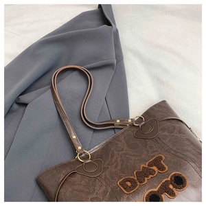 Detail of dark brown tote bag featuring vintage cracked leather texture and plush embroidery