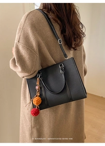 Detail of black textured tote bag with orange and red plush charms on adjustable strap
