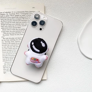 Cute white plush astronaut phone grip and stand on an iPhone case shown from 45-degree angle