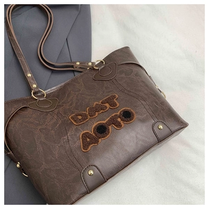 Detail of dark brown tote bag featuring plush letter patches and rivet accents