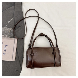 Detailed view of dark brown glossy leather crossbody bag with knot buckle and top handle