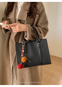Detailed view of black tote bag with textured surface and colorful pompom charm decoration